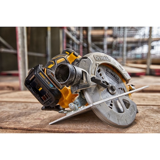A close-up view of a DEWALT cordless circular saw placed on a wooden surface at a construction site, showing the blade and battery pack.