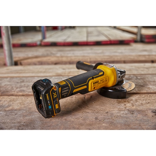 A DEWALT cordless angle grinder with a yellow and black design is resting on a wooden surface at a construction site.