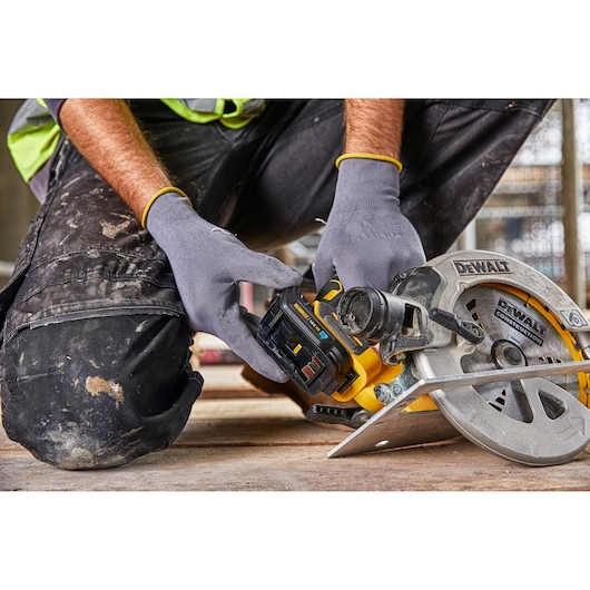 Person wearing gloves and work clothes installing a battery pack into a DEWALT cordless circular saw at a construction site.