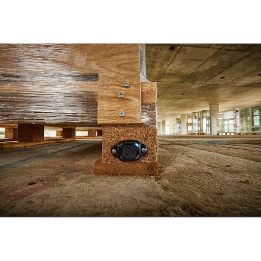 A close-up view of a DEWALT asset tracking device attached to the wooden leg of a pallet in a construction site environment.