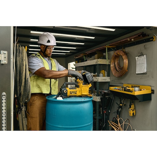 Worker using DEWALT DCE050N tool on a drum inside a workshop, surrounded by cables, shelves, and equipment.