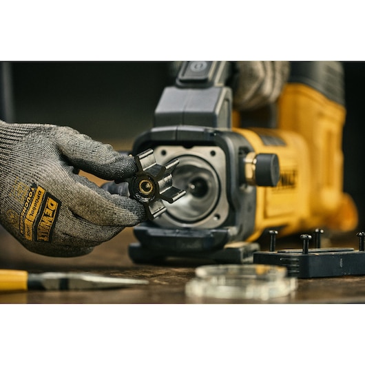 Gloved hand holds part near a yellow DEWALT tool on a workbench with other components and tools visible.