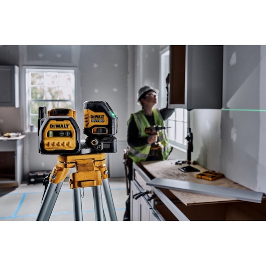 DEWALT laser tool (DCE088D1G18-QW, DCE088D1G18) in use at a construction site on tripod, worker in background.