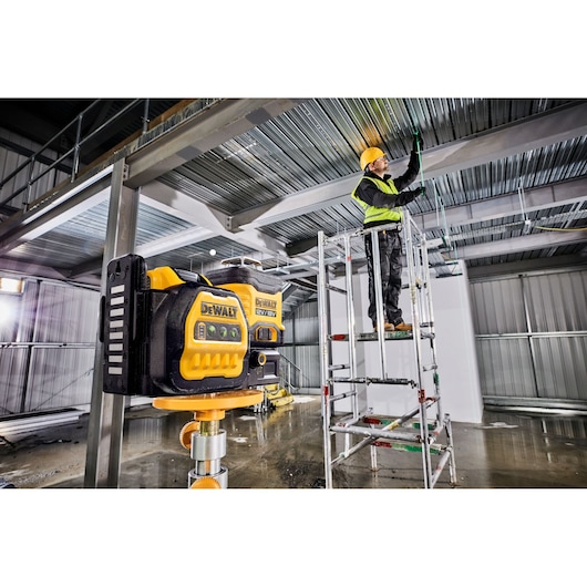 DEWALT laser tool in use at a construction site inside, worker on scaffold adjusting ceiling wiring.