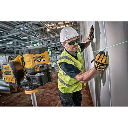 DEWALT laser level projects green lines on wall, worker marks alignment wearing gloves and hard hat at construction site.