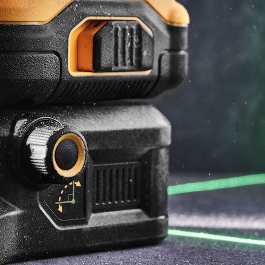 Close-up of a DEWALT laser level tool with green laser lines and adjustment knob, used for precise alignment.
