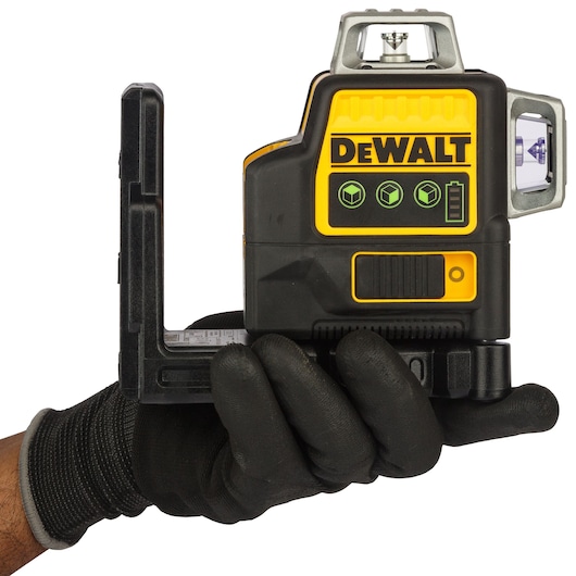 A gloved hand holding a DEWALT green laser level device, model DCE089D1G-QW, with a prominent DEWALT logo and control panel visible on the side.