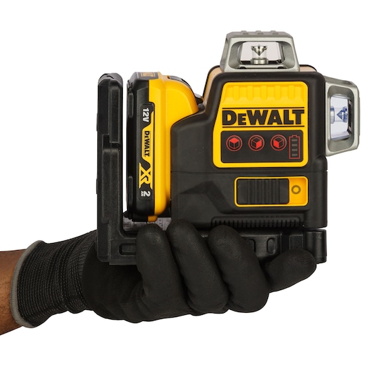 A DEWALT 12V cordless laser level being held in a gloved hand. The device is mainly black and yellow, featuring the DEWALT logo and control buttons on its side.