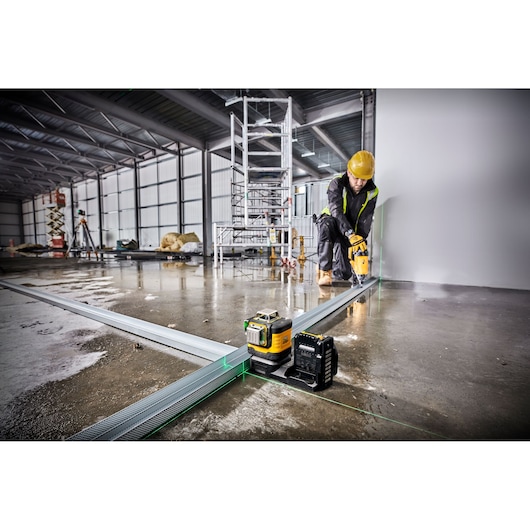DEWALT laser level in use at a construction site, worker in safety gear aligning metal framing on a wet floor.