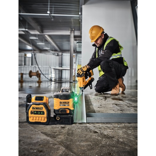 DEWALT DCE089NG18 laser level and tool on a construction site with a worker installing metal framing.