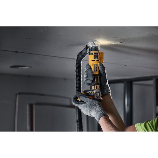 Hand using DEWALT drywall cut-out tool to cut a circular hole in a ceiling panel.