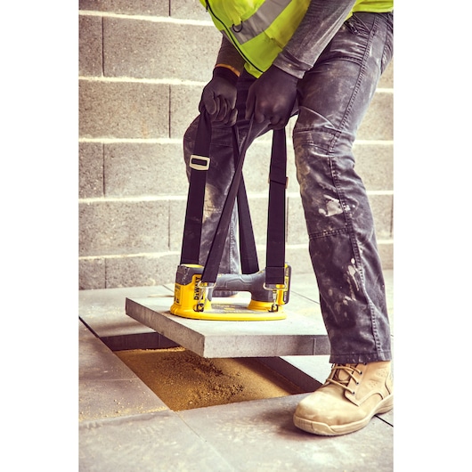 Person using a DEWALT tool to lift a concrete slab with straps at a construction site.