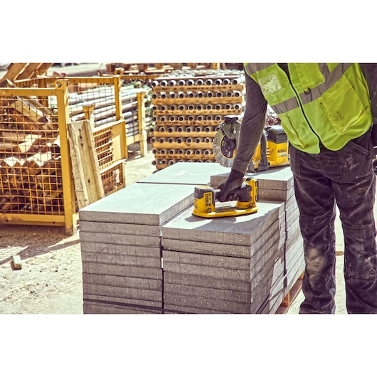 Worker uses DEWALT tool on stacked concrete blocks at construction site, wearing a high-visibility vest.
