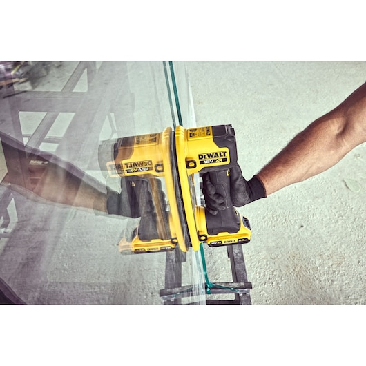 Gloved hand uses yellow DEWALT tool to lift a glass pane, shown in an industrial setting.