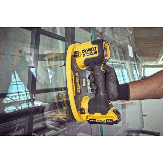 DEWALT cordless glass lifter tool with suction, being used to lift a sheet of glass in an indoor setting.