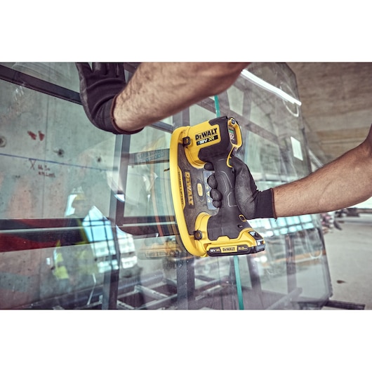DEWALT cordless tool in use, gripping glass with suction pad during installation, worker wearing gloves.