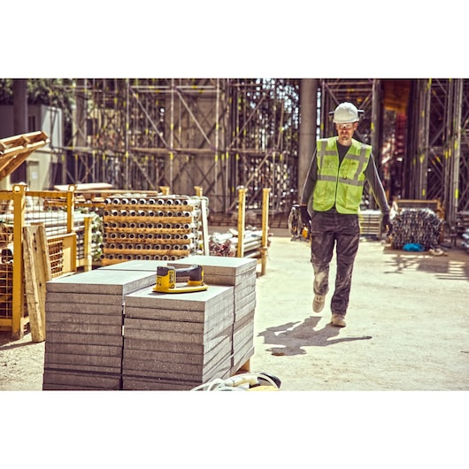 DEWALT DCE590 tool on stacked concrete slabs at a construction site, worker in safety gear nearby.