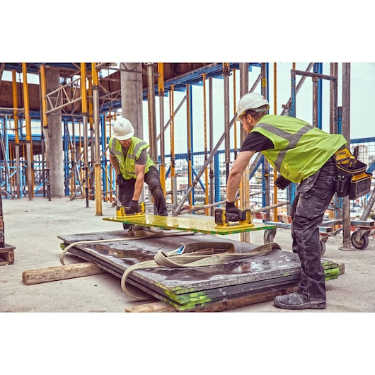 Two workers use DEWALT tools to lift a panel at a construction site. They wear safety gear and high-visibility vests.