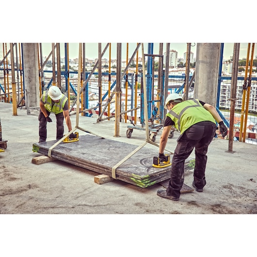Two workers in safety gear using DEWALT tools to lift large panels at a construction site.