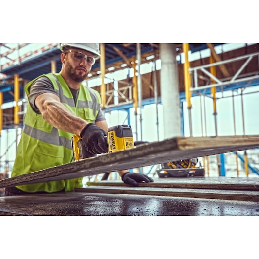 Worker using a DEWALT tool on a construction site with scaffolding in the background.