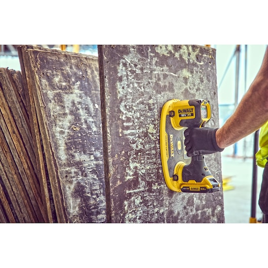 DEWALT cordless tool being used to clean or sand a large, weathered wooden panel at a construction site.