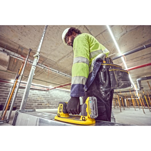 Worker using DEWALT DCE590 tool in industrial setting with safety gear and tool belt.