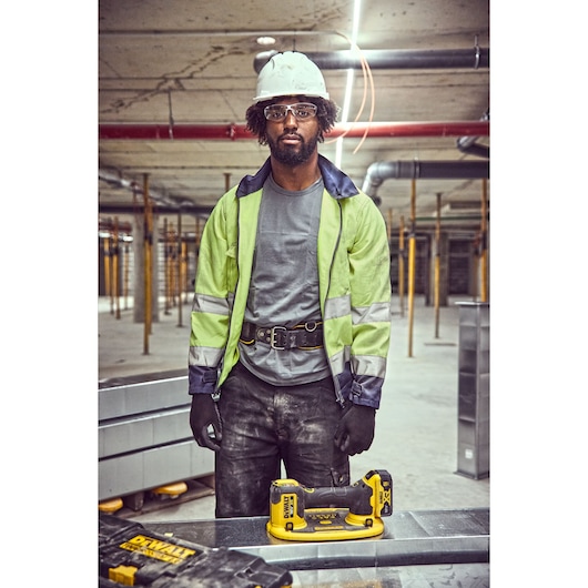 Dewalt DCE590 tool on table, worker in safety gear and hard hat at construction site, industrial background.