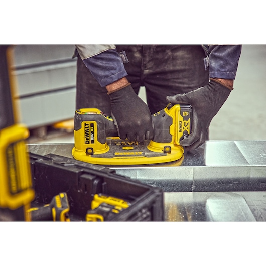 Gloved hands operate a DEWALT DCE590 cordless tool on a metal surface in a workshop.