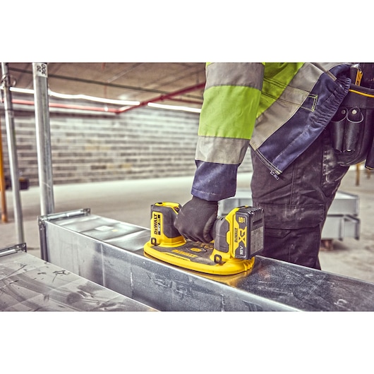 Worker uses DEWALT DCE590 cordless tool on metal surface at construction site.