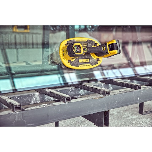 DEWALT DCE590 glass lifter attached to a glass sheet on a metal frame in an industrial setting.