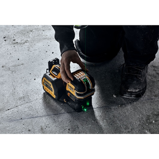 DEWALT laser level placed on concrete floor, operator activates green laser line for alignment.