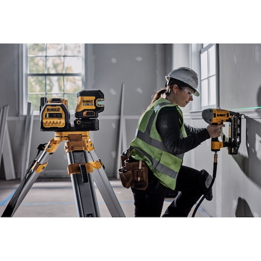DEWALT laser on tripod and worker using DEWALT tool to install wall trim in construction site.
