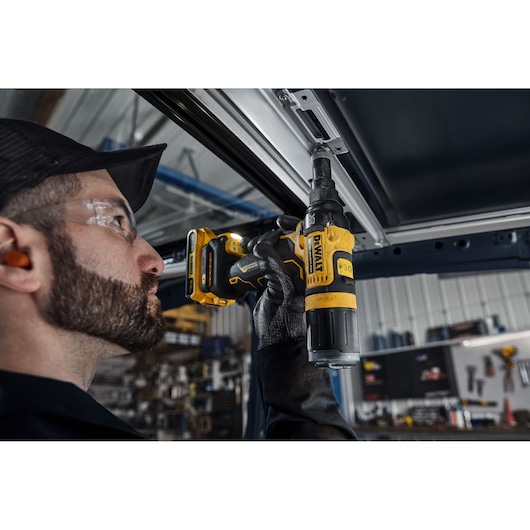 A person using a DEWALT DCF403NT cordless screwdriver to fasten a screw into a metal frame in a workshop setting. The focus is on the tool and the user’s gloved hand.