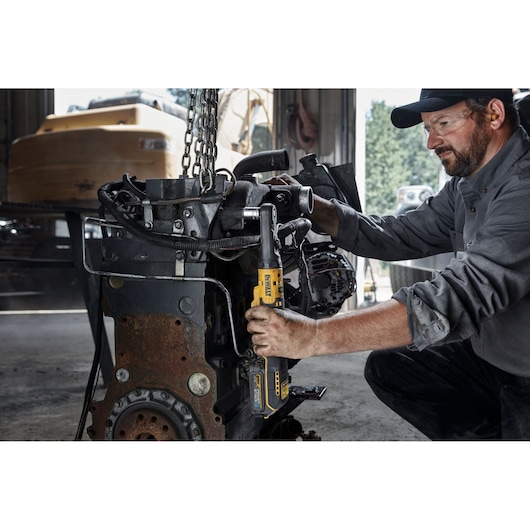 Person uses DEWALT cordless ratchet tool on machinery part in workshop setting.