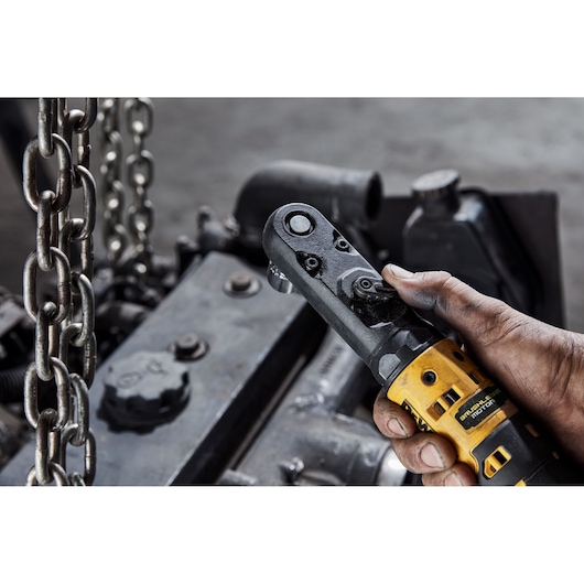Hand holding a DEWALT ratchet tool near chains and machinery in an industrial setting.