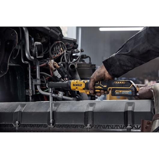 Person using a DEWALT cordless ratchet tool to work on machinery in an industrial setting.