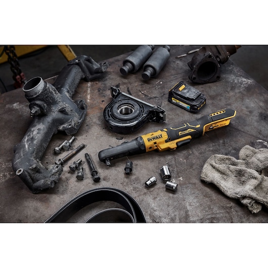 DEWALT cordless ratchet tool, battery and automotive parts on a workshop table with bolts and sockets.