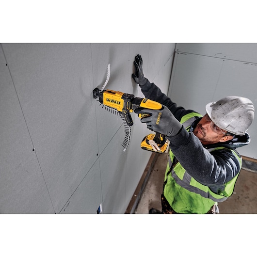 Person using a DEWALT DCF6202 screw gun to attach drywall panels at a construction site. Face is blurred for privacy.