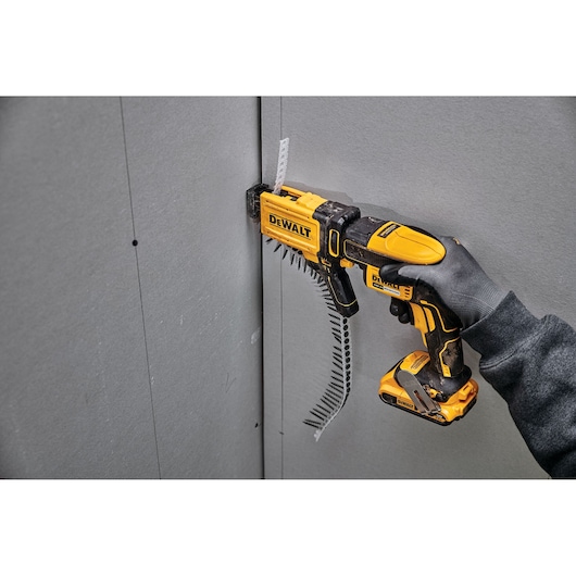 DEWALT DCF6202 screw gun driving screws into drywall, held by a gloved hand against a wall panel.