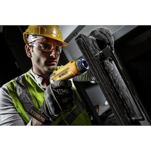 Person using a DEWALT electric screwdriver on a dark surface, wearing gloves and safety gear.