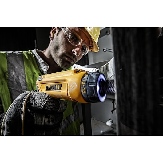 Person using yellow DEWALT DCF680G2 screwdriver with glove in industrial setting.