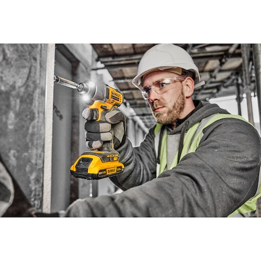 A person wearing a hard hat and safety vest is using a DEWALT cordless impact driver (model DCF840D2T) on a construction site.