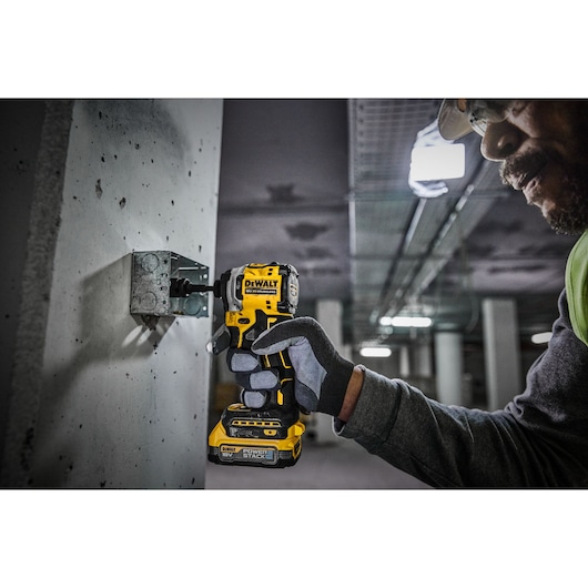 A person wearing gloves and safety gear is using a DEWALT DCF850E2T cordless impact driver to secure a metal bracket to a