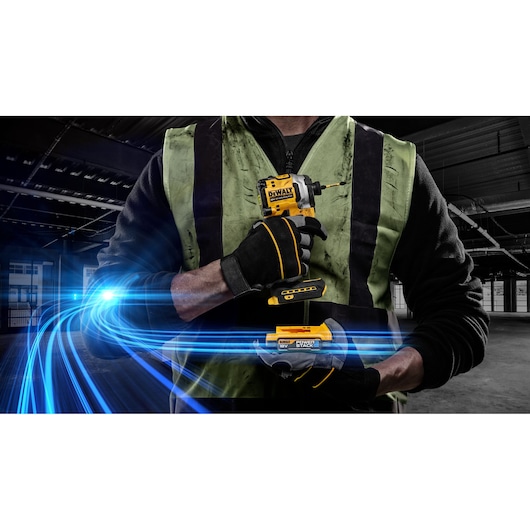 Worker in gloves holding DEWALT DCF850E2T impact driver with POWERSTACK battery, blue light effect in background.