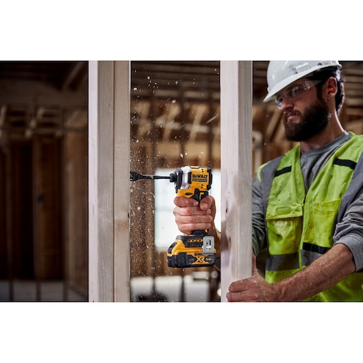 Person using DEWALT DCF850NT drill to bore a hole in a wooden frame on a construction site.