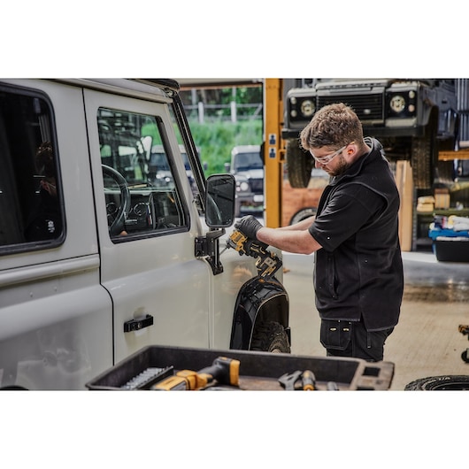 Person uses a DEWALT DCF850NT drill on a white vehicle in a workshop. Tools and equipment are visible in the scene.