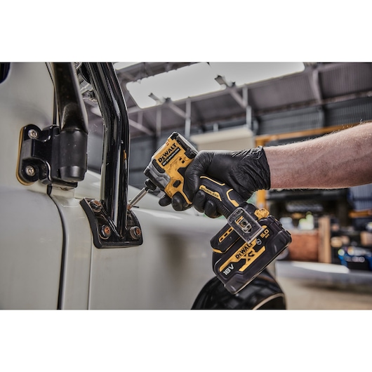 Person uses a DEWALT DCF850NT impact driver to fasten bolts on a vehicle frame in a workshop setting.