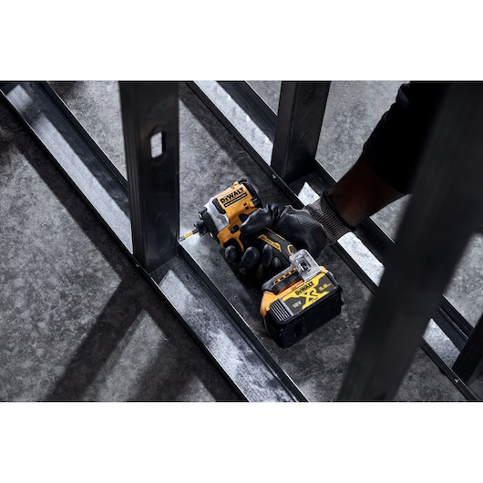 Gloved hand using a DEWALT cordless impact driver on steel framing indoors.