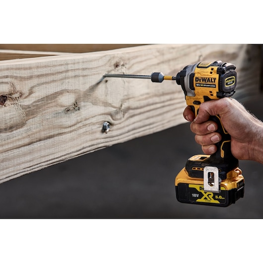 DEWALT cordless impact driver used to drive a screw into a wooden beam. Close-up of the tool held in hand.