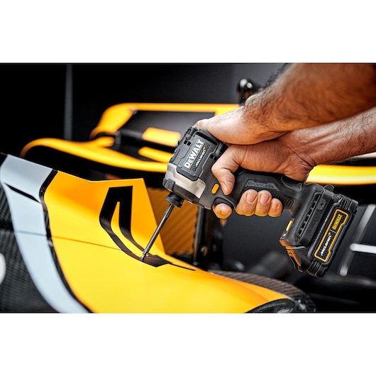 A person uses a DEWALT cordless impact driver to fasten a screw on the yellow bodywork of a vehicle.